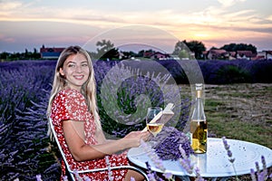 A beautiful woman enjoys a good book, and a glass of wine in a lavender field.
