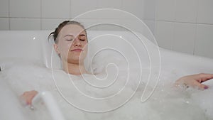 Beautiful woman enjoys the procedure of hydromassage in a special bath with foam.