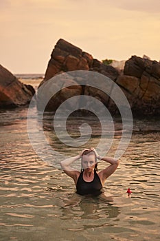 Beautiful woman enjoys serene sea swim at sunset, merges with nature. Wets hair, relaxation in calm waters, symbolizes