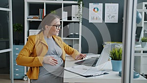 Beautiful woman expecting baby working with laptop computer in modern office