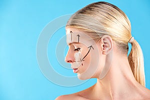 Beautiful Woman Face. Beauty Portrait of young woman blond, painted lines on the face for cosmetic surgery on blue