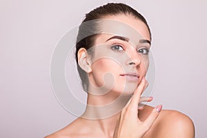 Beautiful woman face close up hand touching face studio on gray