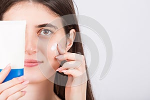 Beautiful woman face closeup portrait applying moisturizer on her cheek isolated on white background. Girl showing a cream tube to