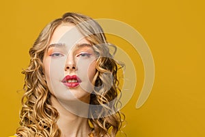Beautiful woman face. Female model with long curly hair on yellow background