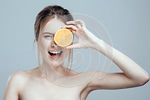 Beautiful woman face with juicy orange on grey background. Natural beauty and spa.