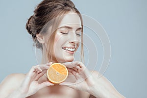 Beautiful woman face with juicy orange on grey background. Natural beauty and spa.