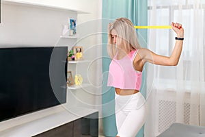 Beautiful woman in fashion sporty clothes making exercize with yellow band at home. Concept home workouts