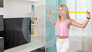 Beautiful woman in fashion sporty clothes making exercize with yellow band at home. Concept home workouts