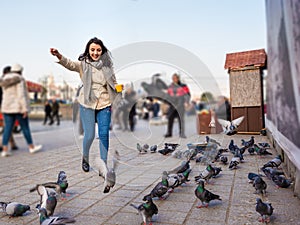 Beautiful woman in fashionable modern clothes feeds pigeons