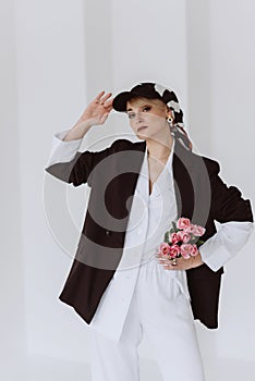 A beautiful woman in a fashionable outfit, a light white suit and a black jacket, a baseball cap and with a bouquet of tulips in