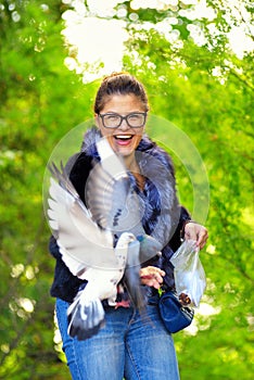 Beautiful woman feeds pigeons in autumn park and laughs