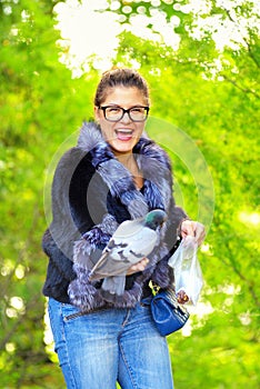 The beautiful woman feeds pigeons in autumn park and laughs