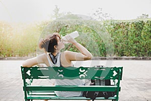 Beautiful woman feel tried and thirsty, itâ€™s sunny day. Charming beautiful girl sit on bench at park and take a rest, feel