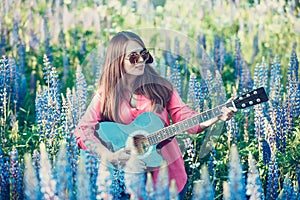 Beautiful woman in the field with lupine playing guitar