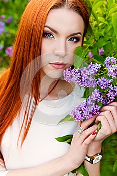 Beautiful woman with fiery regime hair with eyes of a Fox in the garden with lilacs