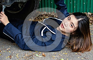 A beautiful woman is fixing machine under car