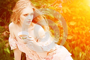 Beautiful woman with flowering tree drinking tea in sunset in sp