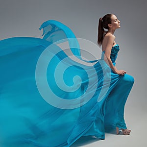 Beautiful woman in fluttering airy blue dress. Gray background.