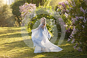 Beautiful woman in flying airy blue dress in blooming lilac garden.