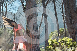 Woman dancing in a forest flicking her hair with trees in the background.