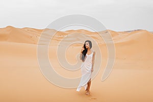 Beautiful woman in gentle silk dress walking sand dunes of Morocco Sahara desert