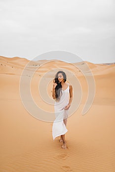 Beautiful woman in gentle silk dress walking sand dunes of Morocco Sahara desert
