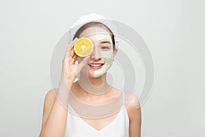 Beautiful woman is getting facial clay mask and holding orange pieces on white background. Beauty, body care and spa concept