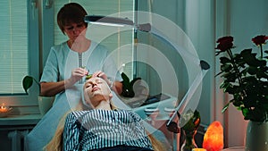 Beautiful woman getting facial massage with jade roller at beauty salon with dim light around