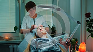Beautiful woman getting facial massage with jade roller at beauty salon with dim light around