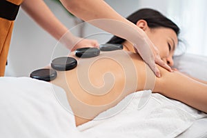 Beautiful woman getting spa hot stone massage in the therapy room at wellness center. Masseuse or physical therapist doing massage