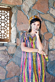 Beautiful woman, girl in national folk Uzbekistan dress against stone wall and ancient window background