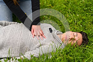 Beautiful woman giving first aid to a handsome young man, cardiopulmonary resuscitation, in a grass background