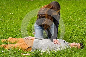 Beautiful woman giving first aid to a handsome young man, cardiopulmonary resuscitation, in a grass background