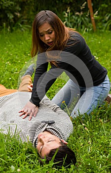 Beautiful woman giving first aid to a handsome young man, cardiopulmonary resuscitation, in a grass background
