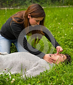 Beautiful woman giving fisrt aid to a handsome young man, cardiopulmonary resuscitation, in a grass background