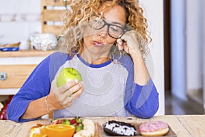 Beautiful woman with glasses choosing green apple of donuts - healthy and sane lifestyle concept