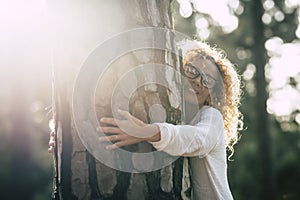 Beautiful woman with glasses hugging a big tree with love and affection - save the forest concept and lifestyle - adult at the