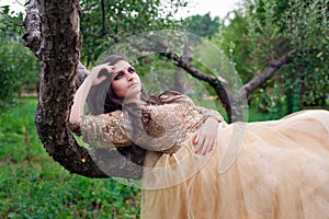 Beautiful woman in gold dress is lying on the tree