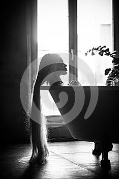 A beautiful woman with gorgeous long blond hair is relaxing in the bath. Silhouette of a woman in profile lying in the bathroom