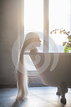 A beautiful woman with gorgeous long blond hair is relaxing in the bath. Silhouette of a woman in profile lying in the bathroom
