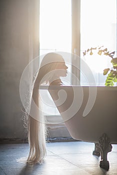 A beautiful woman with gorgeous long blond hair is relaxing in the bath. Silhouette of a woman in profile lying in the