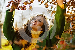 beautiful woman with a gorgeous white-toothed smile lifting up her head and hands touching the yellow leaves in the park