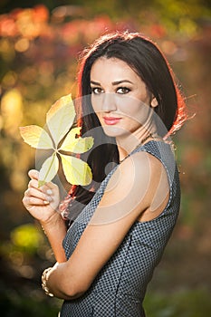Beautiful woman in gray posing in autumnal park. Young brunette woman holding a leaf and spending time in autumn