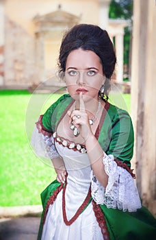 Beautiful woman in green medieval dress making silence gesture