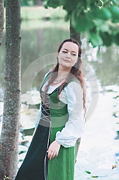 Beautiful woman in green medieval dress near river