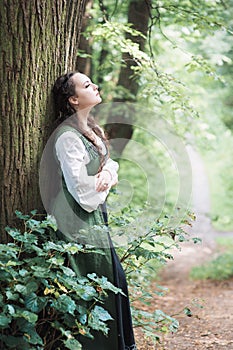 Beautiful woman in green medieval dress near tree