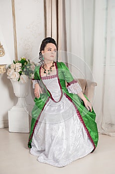 Beautiful woman in green rococo style medieval dress sitting in the armchair