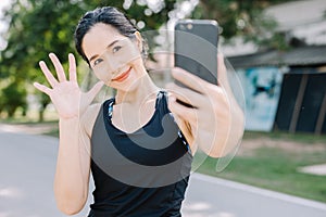 A beautiful woman in the gym stands with a smartphone smiling and looks at the screen outside the building during the day.