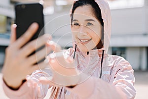 A beautiful woman in the gym stands with a smartphone smiling and looks at the screen outside the building during the day.