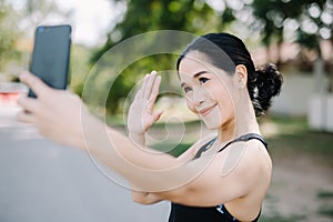 A beautiful woman in the gym stands with a smartphone smiling and looks at the screen outside the building during the day.